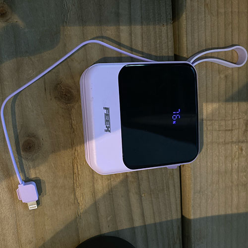 front view of A purple power bank with charging cable out and charging percentage display on